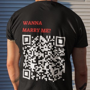 Peut inclure: T-shirt noir avec le texte "Wanna Marry Me?" et un code QR noir et blanc imprimé au dos.