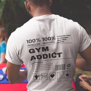 May include: White t-shirt with black text that reads "100% Muscles 100% Natural" and "Gym Addict". The text is in a label format with a barcode and other icons.