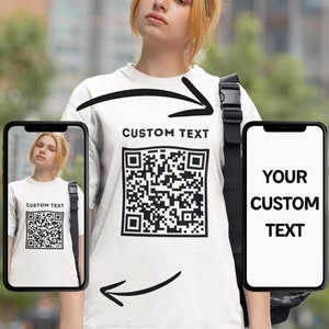 Può includere: Maglietta bianca con un codice QR nero e il testo "CUSTOM TEXT" stampato sul davanti. Una persona indossa la maglietta e tiene uno smartphone con un design simile.