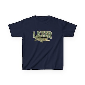 May include: Navy blue t-shirt featuring the word "LATER" in green, textured lettering above a cartoon alligator with an open mouth. The alligator is green and tan. The shirt is a short-sleeved crew neck.