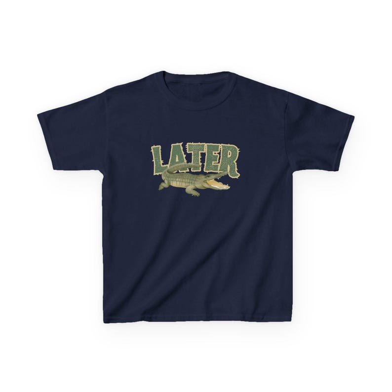 May include: Navy blue t-shirt featuring the word "LATER" in green, textured lettering above a cartoon alligator with an open mouth. The alligator is green and tan. The shirt is a short-sleeved crew neck.