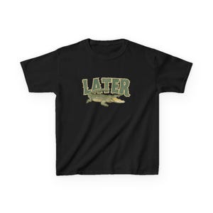 May include: Black t-shirt featuring a green alligator graphic with the word "LATER" in a matching green, textured font. The alligator is depicted with its mouth open. The shirt is a casual wear item.