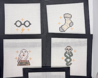 May include: Five square needlepoint canvases with black taped borders. The designs feature black round glasses with a lightning bolt, a striped sock, a white owl perched on books, a green snake coiled around a skull, and a black triangular symbol.