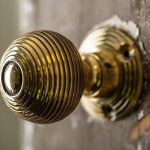 May include: A gold door knob with a round, ribbed design. The knob is attached to a round, flat base.