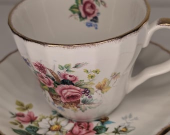 Può includere: Una tazza da tè e un piattino bianchi con un bordo dorato. La tazza e il piattino sono decorati con un motivo floreale con fiori rosa, gialli e verdi.