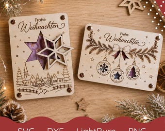 May include: Two rectangular light-colored wooden plaques with laser-engraved designs. One features a star cutout and a winter village scene with the text Frohe Weihnachten. The other shows three hanging ornaments and pine branches with the text Frohe Weihnachten.
