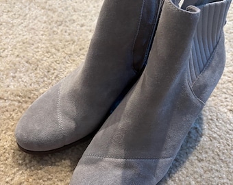 May include: A pair of gray suede ankle boots with a side zipper and a ribbed knit collar. The boots have a rounded toe and a low heel. The boots are displayed on a beige carpet.