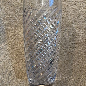 May include: A clear, tall glass with a spiral-cut design. The glass has a thick base and a cylindrical shape, perfect for serving beverages. The intricate pattern catches the light, adding a touch of elegance.