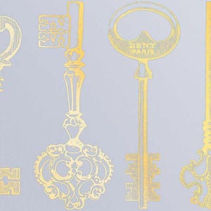 Op de afbeelding: Vier gouden sleutels met ingewikkelde ontwerpen. De sleutels hebben verschillende vormen en maten. De sleutel rechts heeft de tekst "DENY PARIS" erop.