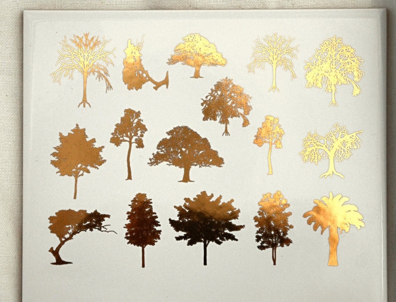 May include: A sheet of gold foil stickers featuring various tree silhouettes. The trees are in different styles and sizes, including palm trees, oak trees, and pine trees.