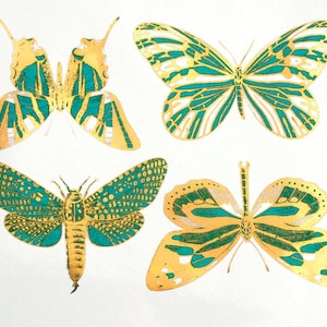 May include: Four gold foil butterflies with green and white accents on a white background. The butterflies are in different sizes and positions.
