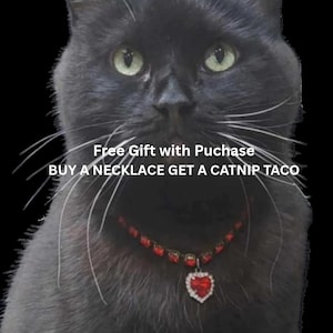 May include: A black cat with green eyes wearing a red heart-shaped pendant necklace. The image includes the text "Free Gift with Purchase" and "BUY A NECKLACE GET A CATNIP TACO."
