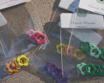 Può includere: Assortimento di ciondoli a forma di fiore di vari colori, tra cui rosa, rosso, giallo, arancione, viola e verde. I ciondoli sono confezionati in sacchetti di plastica trasparente con etichette "Hand Made".