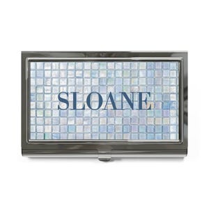 May include: A rectangular metal business card holder with a polished dark gunmetal finish. The front panel features a grid of iridescent, light blue and white square tiles with the name SLOANE printed in bold, dark blue capital letters.
