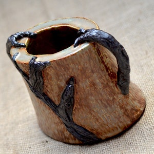 Könnte beinhalten: Eine Keramikvase in Form eines Baumstamms mit schwarzen Ästen. Die Vase hat ein rustikales, erdiges Aussehen und ist perfekt für die Präsentation von Blumen oder anderen Dekorationsartikeln.