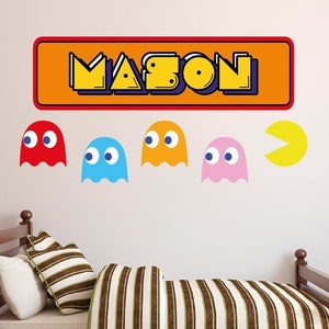 Könnte beinhalten: Ein Wandaufkleber mit dem Namen "MASON" im Retro-Videospiel-Stil, mit vier Pac-Man-Geistern in Rot, Blau, Orange und Pink und einem gelben Pac-Man.