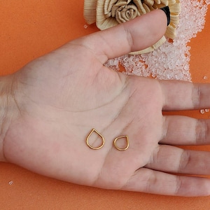 Puede incluir: Dos pendientes de oro en forma de lágrima en una mano.