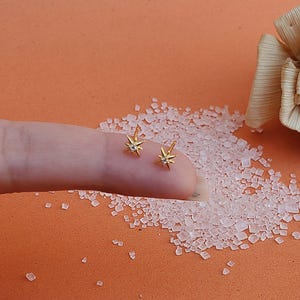 May include: A pair of gold star-shaped earrings with a small clear stone in the centre of each star.