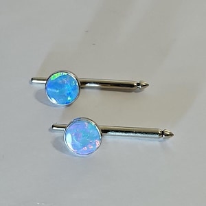 May include: Two silver cufflinks with blue opal stones. The stones have a light blue base with iridescent green and pink hues.