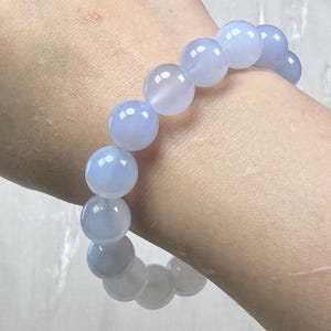 May include: A light blue beaded bracelet. The bracelet features large, round beads with a translucent appearance. The beads are strung together to form a complete circle. The bracelet is worn on a wrist.