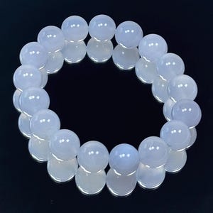May include: A light blue beaded bracelet. The bracelet is made of round, polished beads. The beads have a translucent quality and reflect light. The bracelet is displayed on a reflective black surface.