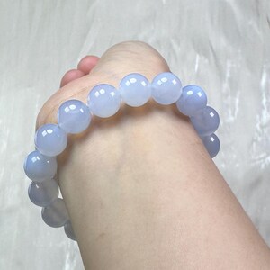 May include: A light blue beaded bracelet. The bracelet is made of large, round, translucent beads. The beads are a soft, pastel blue color and appear to be strung together on an elastic band. The bracelet is shown on a wrist.