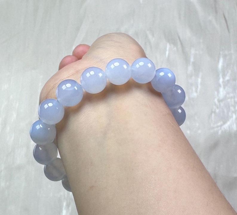 May include: A light blue beaded bracelet. The bracelet is made of large, round, translucent beads. The beads are a soft, pastel blue color and appear to be strung together on an elastic band. The bracelet is shown on a wrist.