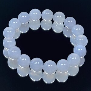 May include: A bracelet made of light blue, round gemstone beads. The beads are strung together to form a circular shape. The bracelet is displayed on a reflective black surface, enhancing the beads' color and shine.