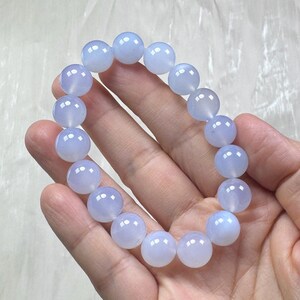 May include: A light blue beaded bracelet. The bracelet is made of round, polished beads. The beads are a soft, translucent blue color. The bracelet is held in a hand.