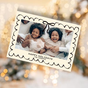 May include: A Christmas card with a photo of a family with two children. The card has a black and white border with a bow at the top. The text "Happy Holidays The Josephs" is printed on the card.