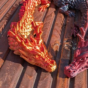 Könnte beinhalten: Eine Sammlung farbenfroher, 3D-gedruckter Drachenfiguren in Rot, Orange, Grün und Schwarz. Die Drachen sind auf einer Holzoberfläche angeordnet und zeigen ihre detaillierten Schuppen und komplizierten Designs.