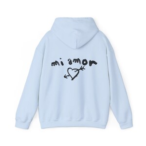 K&ouml;nnte beinhalten: Ein hellblauer Hoodie mit einem schwarzen Grafikdruck auf der R&uuml;ckseite, der "mi amor" mit einem Herz und einem Pfeil sagt.