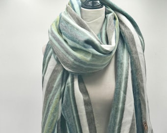 May include: A striped scarf in shades of green, gray, and white is draped over a mannequin. The scarf has a fringed edge and a tag. The vertical stripes create a visual pattern. This accessory is suitable for cool weather.