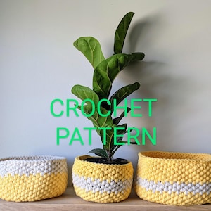 May include: Three handmade crochet plant baskets in yellow and white. The baskets are in different sizes and shapes, with a yellow and white striped design. A green plant is in the center basket. The text "CROCHET PATTERN" is in green.