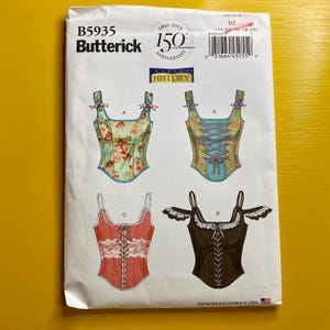 May include: A Butterick sewing pattern, B5935, showcasing four corset designs. The pattern includes a floral print, a lace-up design, and a dark brown corset with decorative trim. The pattern celebrates the 150th anniversary.