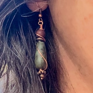 May include: A pair of dangle earrings with a green stone, brown bead, and copper wire wrapping.