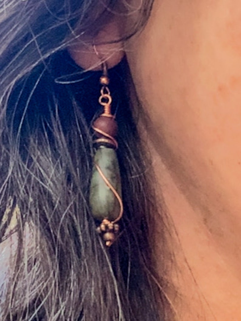 May include: A pair of dangle earrings with a green stone, brown bead, and copper wire wrapping.