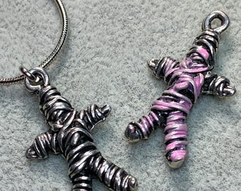 May include: Two silver charm necklaces with mummy figures. One mummy is silver and the other is silver with pink accents.