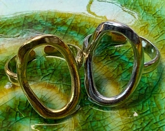 May include: Two simple oval rings, one gold and one silver, on a green and yellow textured surface.