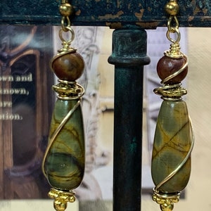 May include: A pair of gold wire wrapped earrings with brown and green stone teardrop dangles. Each earring has a brown bead and gold beads at the top.