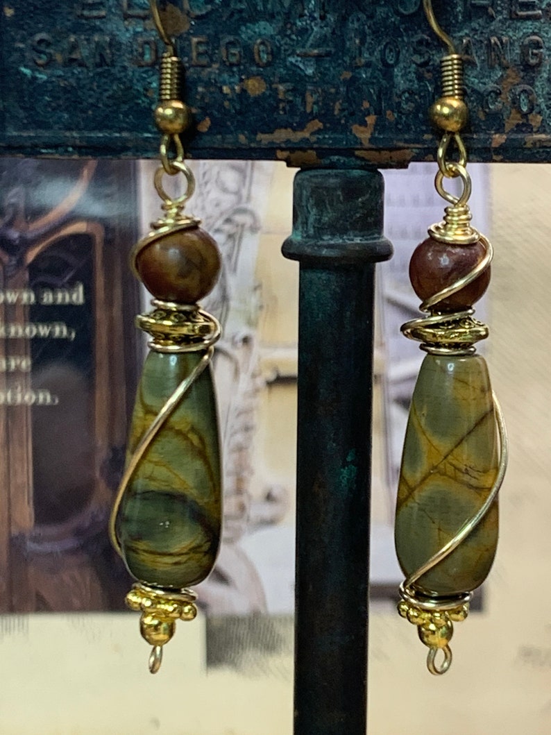 May include: A pair of gold wire wrapped earrings with brown and green stone teardrop dangles. Each earring has a brown bead and gold beads at the top.