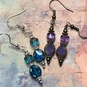 May include: A pair of dangle earrings with purple and blue glass beads. The earrings have silver and bronze accents.