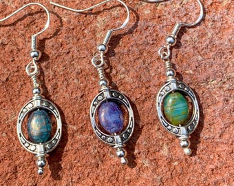 May include: Three pairs of silver dangle earrings with oval-shaped glass beads. The beads are iridescent and have a blue, green, and purple color scheme.
