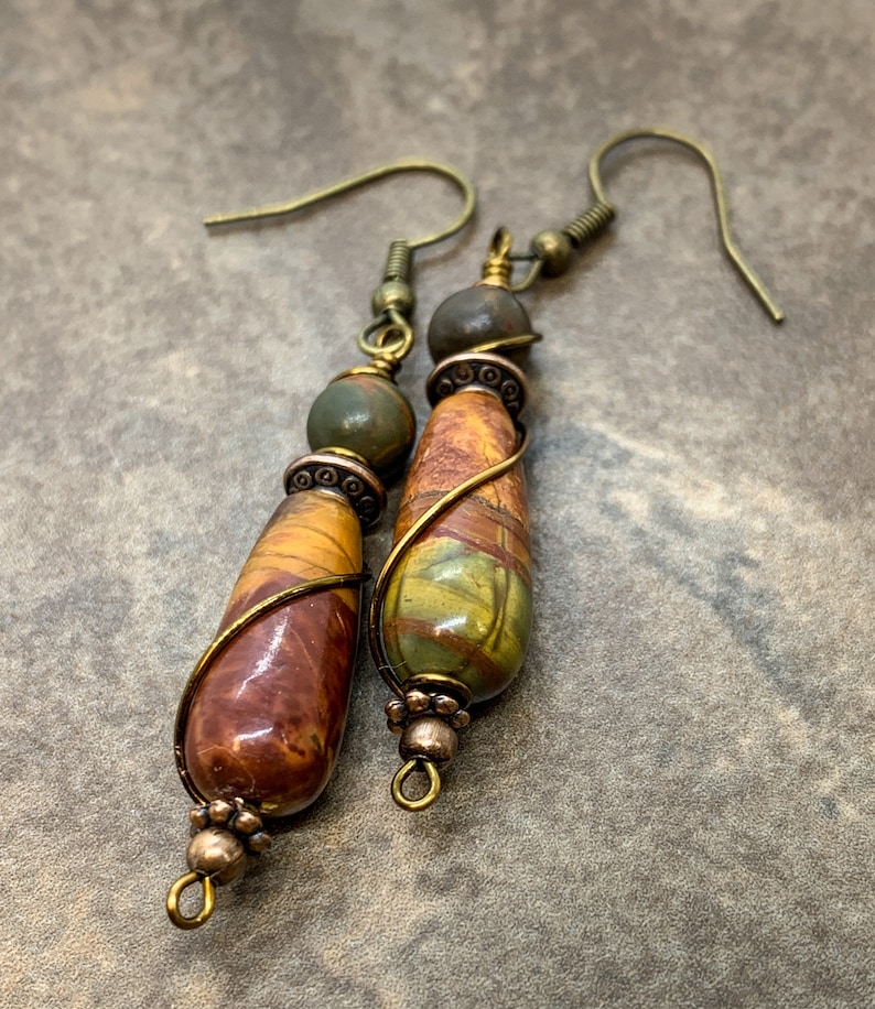 May include: A pair of dangle earrings with brown, green, and gold stone beads wrapped in wire. The earrings have a simple hook closure.