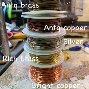 May include: A stack of spools of wire in different colors and finishes, including antique brass, antique copper, silver, rich brass, and bright copper.
