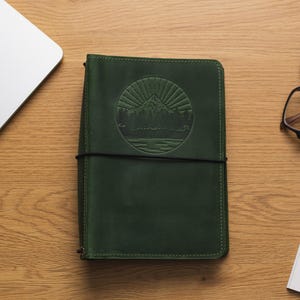 May include: A dark green leather journal with a debossed mountain scene and a black elastic closure.