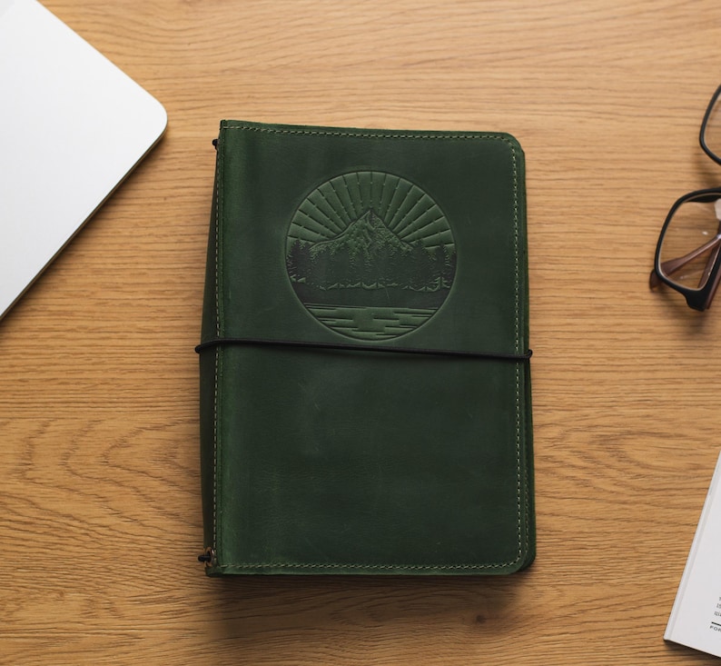 May include: A dark green leather journal with a debossed mountain scene and a black elastic closure.