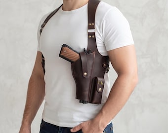 Peut inclure: Un étui d'épaule en cuir marron foncé doté d'un système de sangles sécurisé, de ferrures en métal couleur laiton et d'une pochette intégrée avec les initiales LK gravées sur le rabat. L'étui contient une arme de poing à poignée en bois.