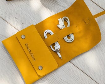May include: Mustard yellow leather cable organizer with a flap closure and two silver snaps. The organizer holds two white charging cables. The text "DonskyStore" is printed on the flap.