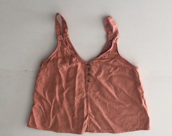 May include: A coral-coloured tank top with a V-neck and button-up front. The top has wide straps and a relaxed fit. The fabric appears to be a lightweight material, suitable for warm weather. The top is a solid colour with no visible patterns.